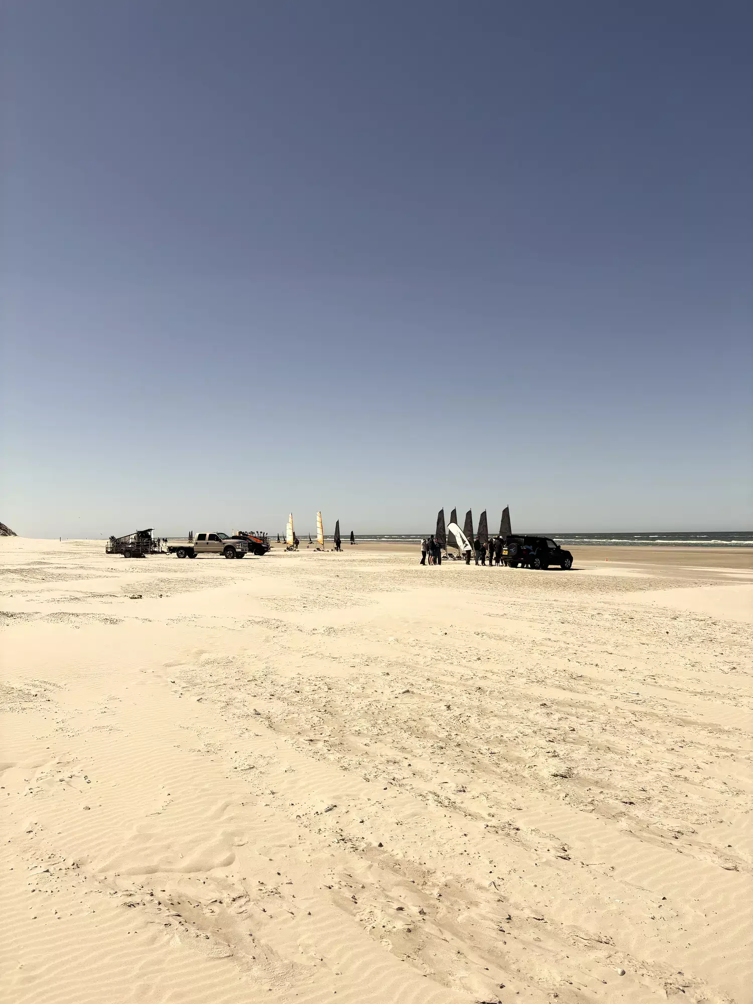 Uitgestrekt zandstrand van Terschelling onder een strakblauwe lucht met blokarts en auto's in de verte