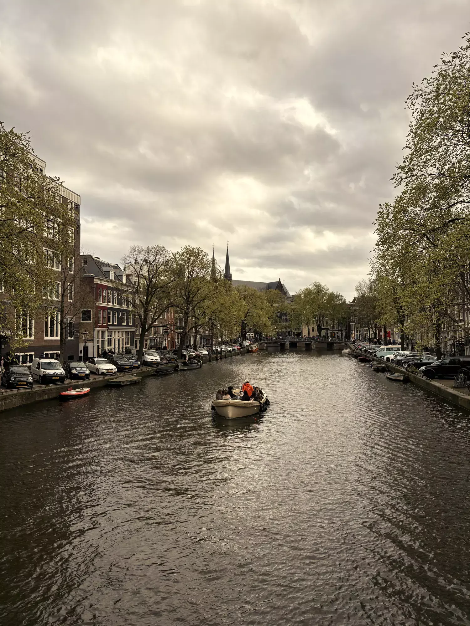 Bootjes varen over een brede Amsterdamse gracht met grachtenpanden en bomen langs de kade