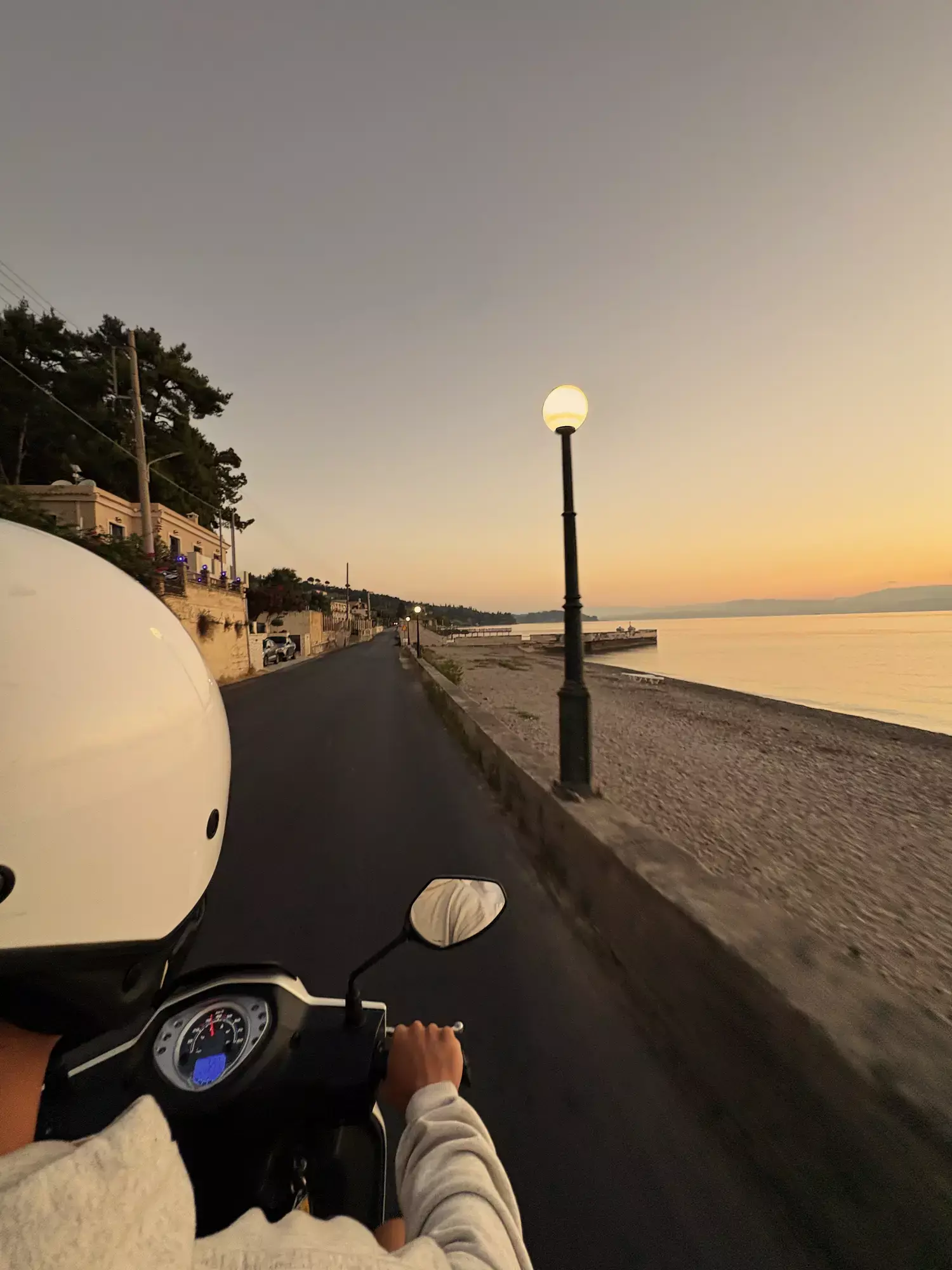 Scooterrit over een kustweg met straatlantaarns langs het strand op Corfu bij zonsondergang