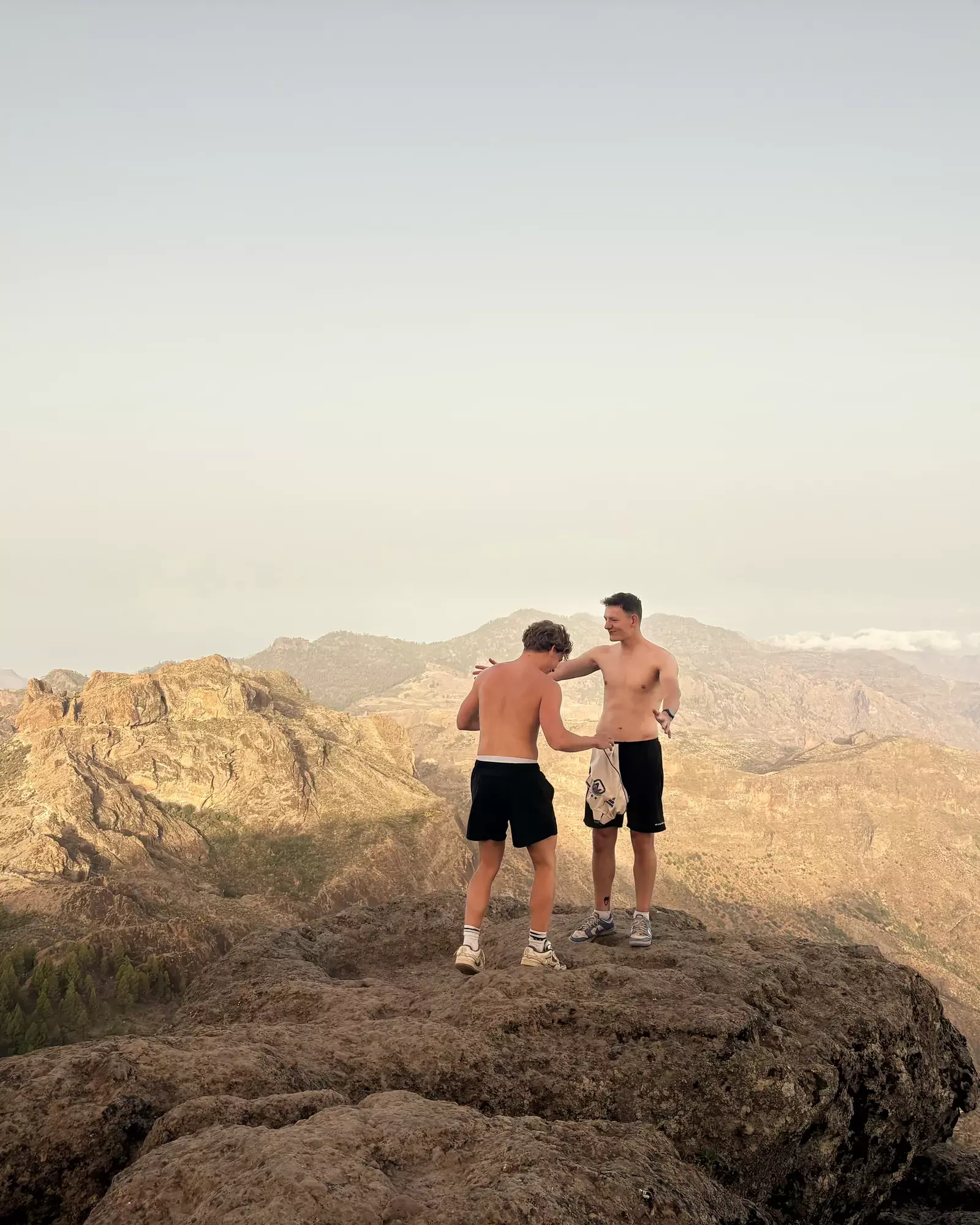Twee jongens zonder shirt op een rotstop bij Roque Nublo, met de bergen van Gran Canaria erachter Roque Nublo