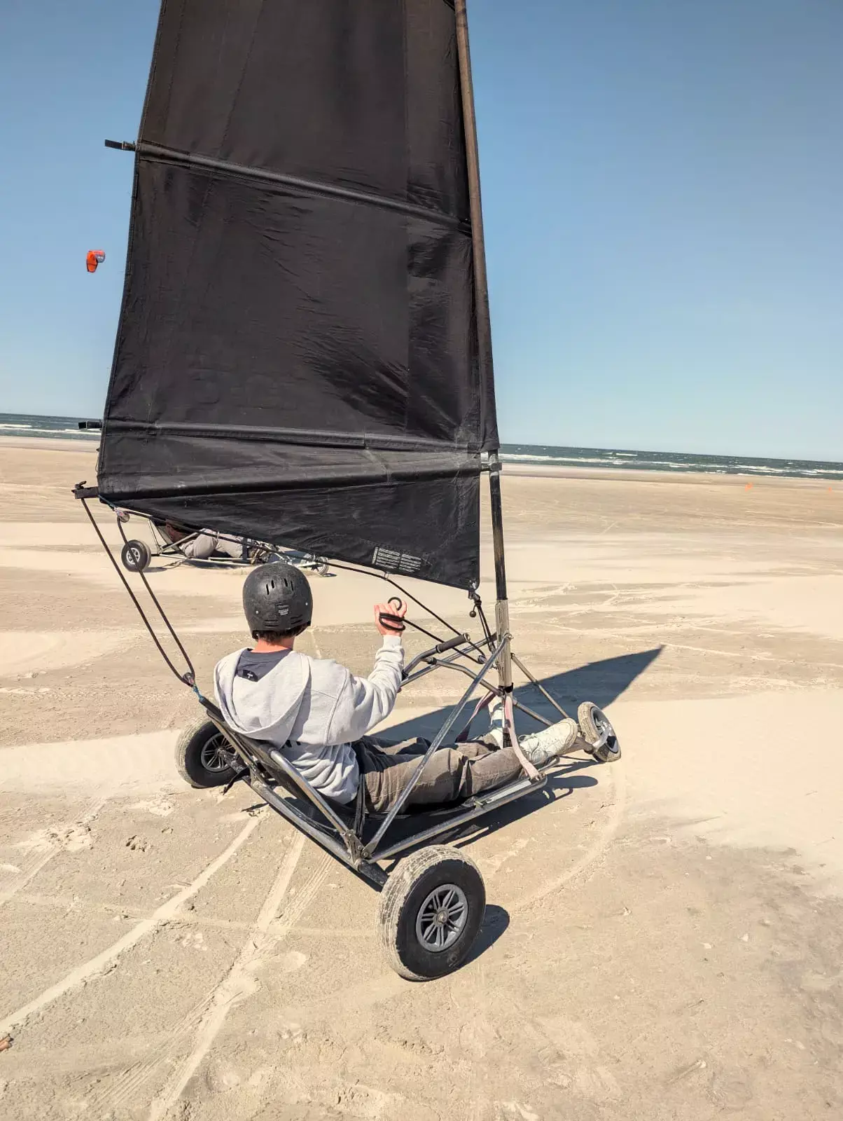 Jongen met helm racet in een blokart met zwart zeil over het brede strand van Terschelling tijdens het blokarten bij MooiWeer
