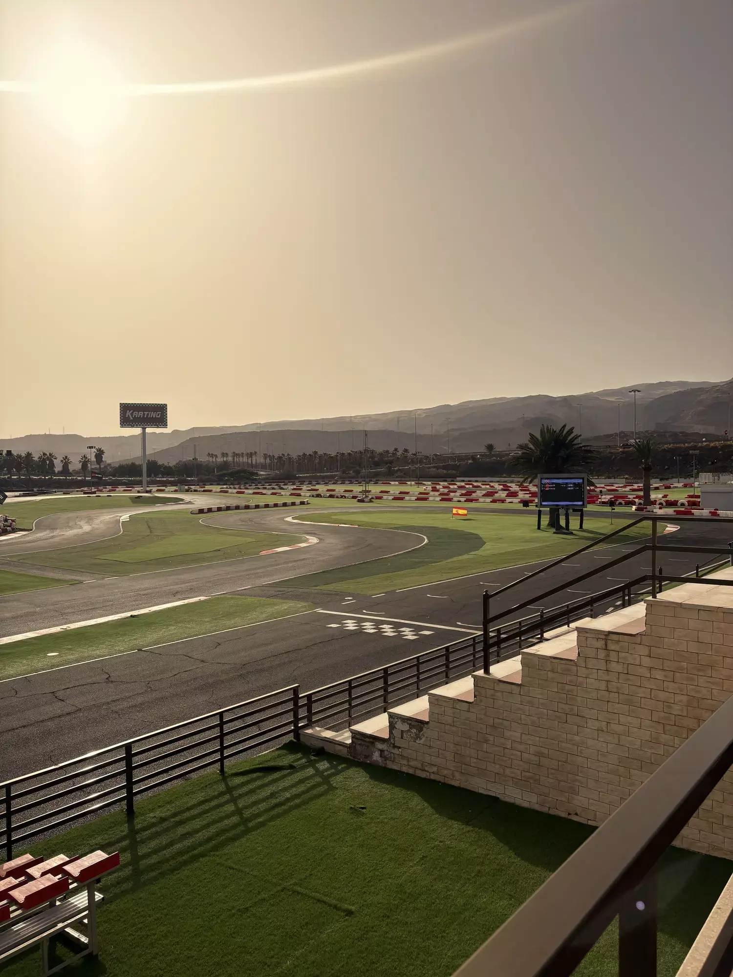 Bochtige kartbaan met geblokte finishlijn en Karting-bord, bergen op de achtergrond bij laagstaande zon