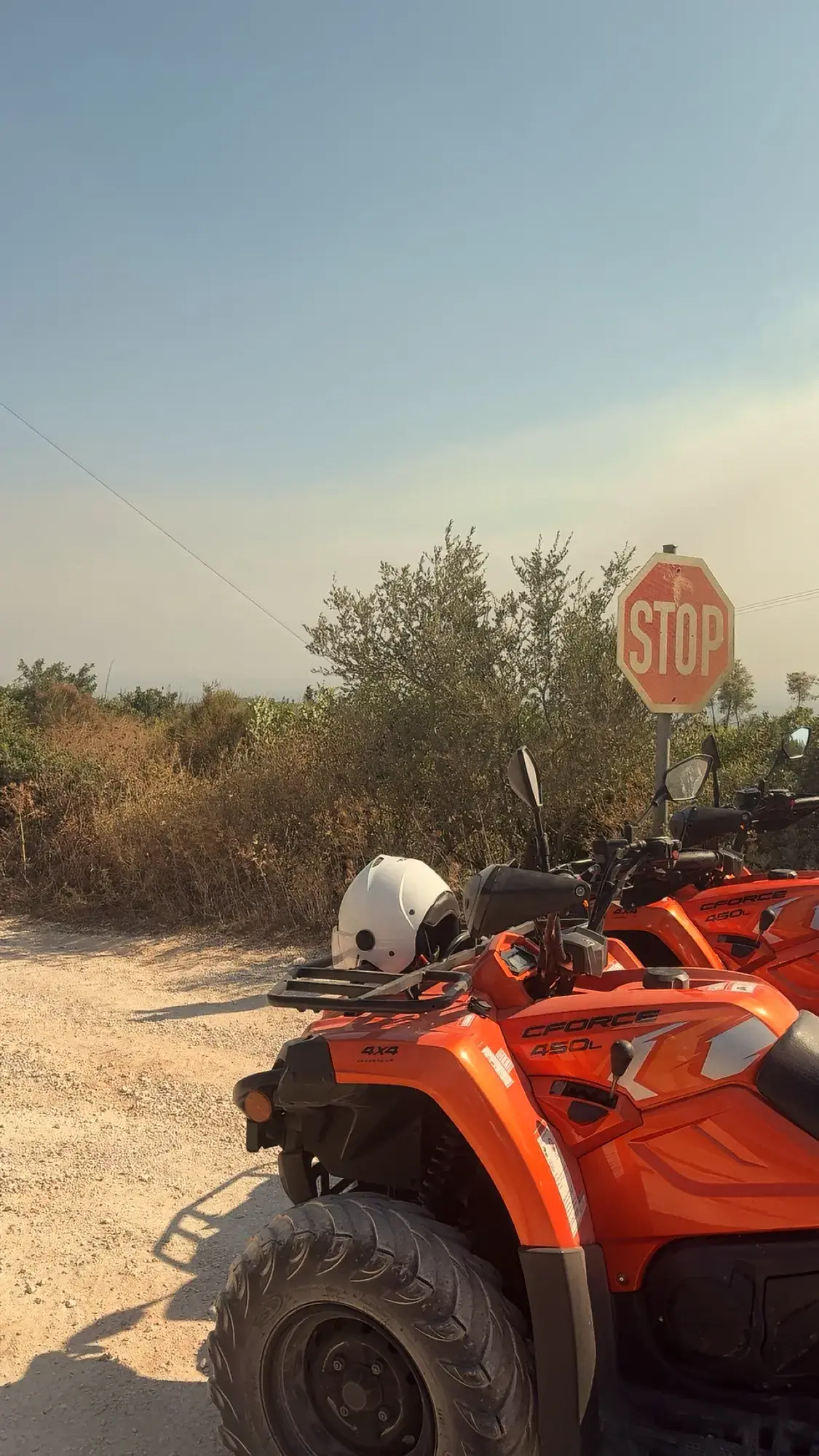 Rij oranje CFORCE 450 quads met helm geparkeerd langs een onverharde weg bij een stopbord op Zakynthos