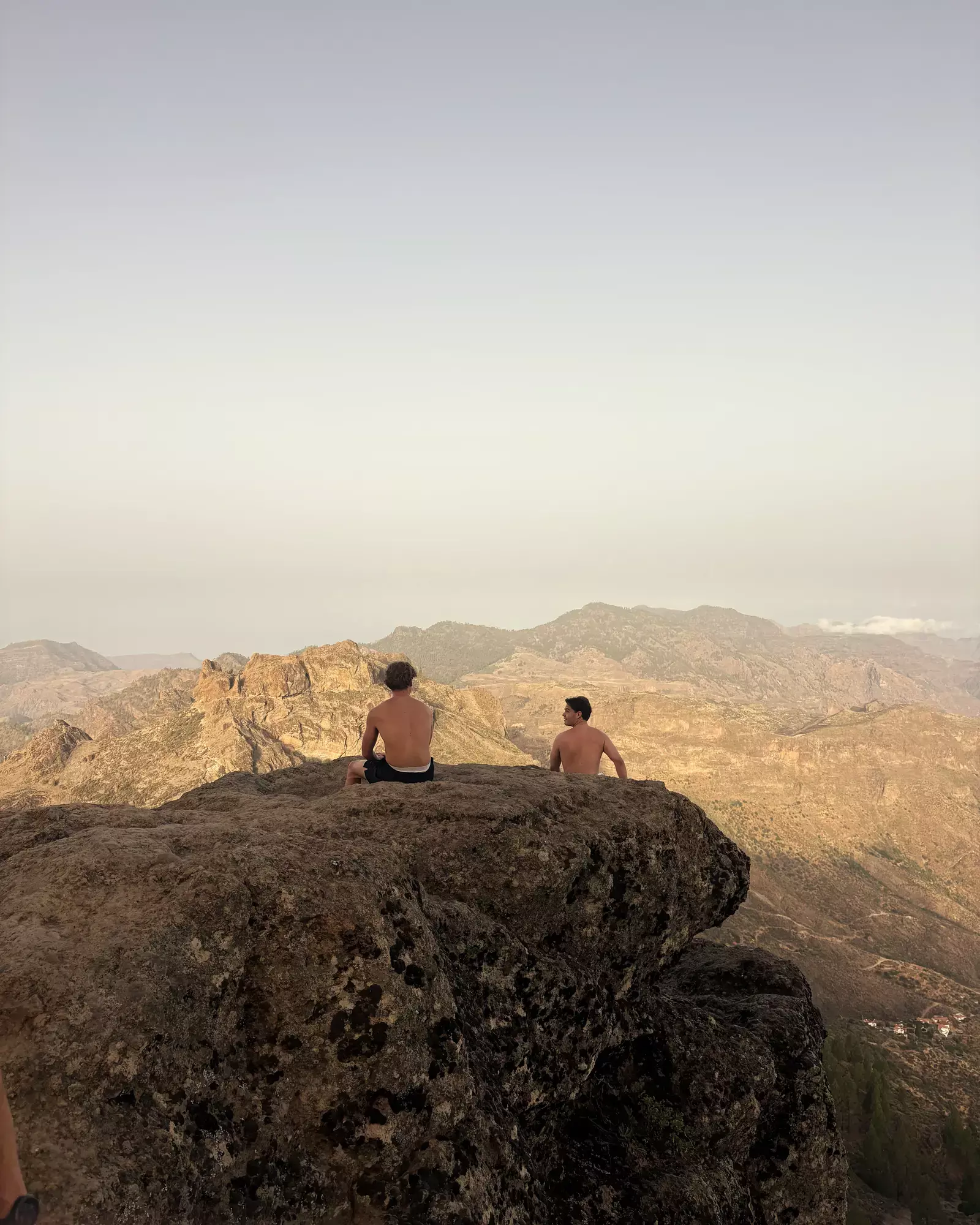 Twee wandelaars zitten op een rotsrand bij Roque Nublo en kijken uit over het berglandschap Roque Nublo