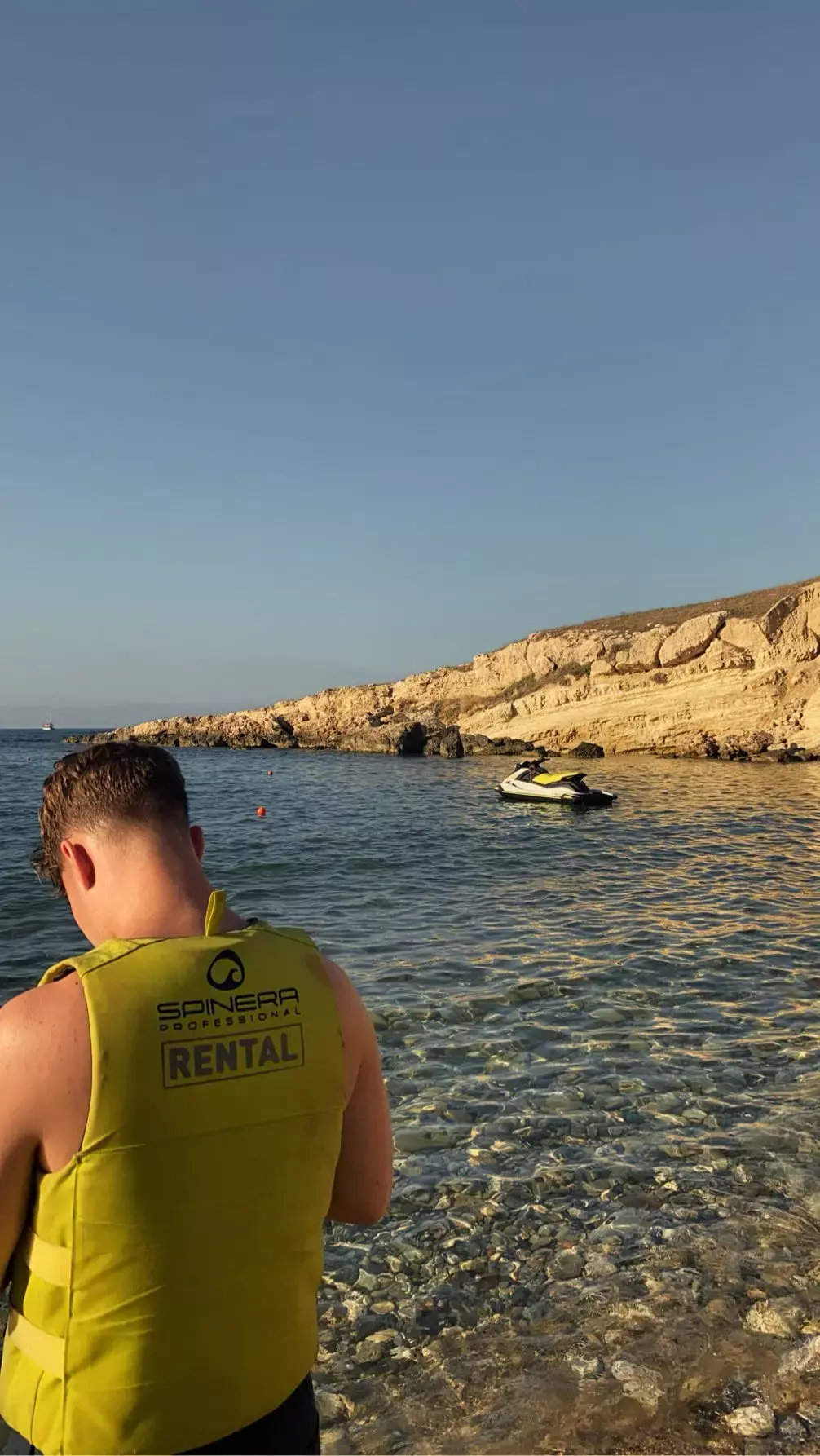 Man in geel huurvest kijkt naar een jetski in een heldere baai met rotskust bij Chersonissos op Kreta