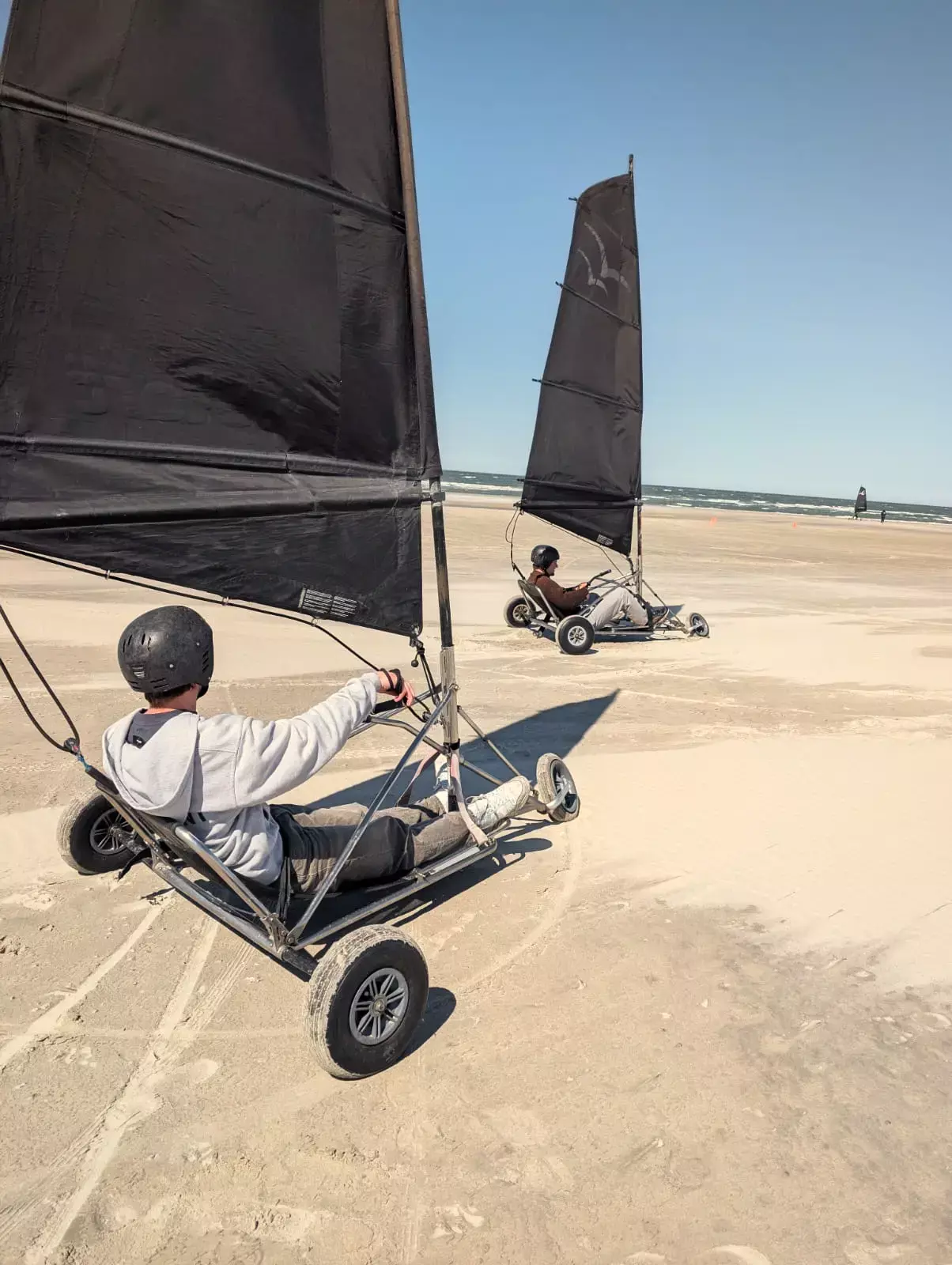 Twee blokarts met zwarte zeilen rijden over het zonnige strand van Terschelling met de Noordzee op de achtergrond