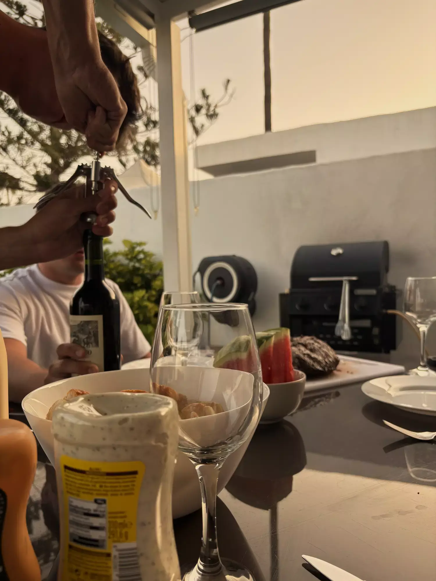 Rode wijnfles wordt geopend aan tafel met wijnglazen, watermeloen en barbecue op het terras van een vakantievilla in Maspalomas