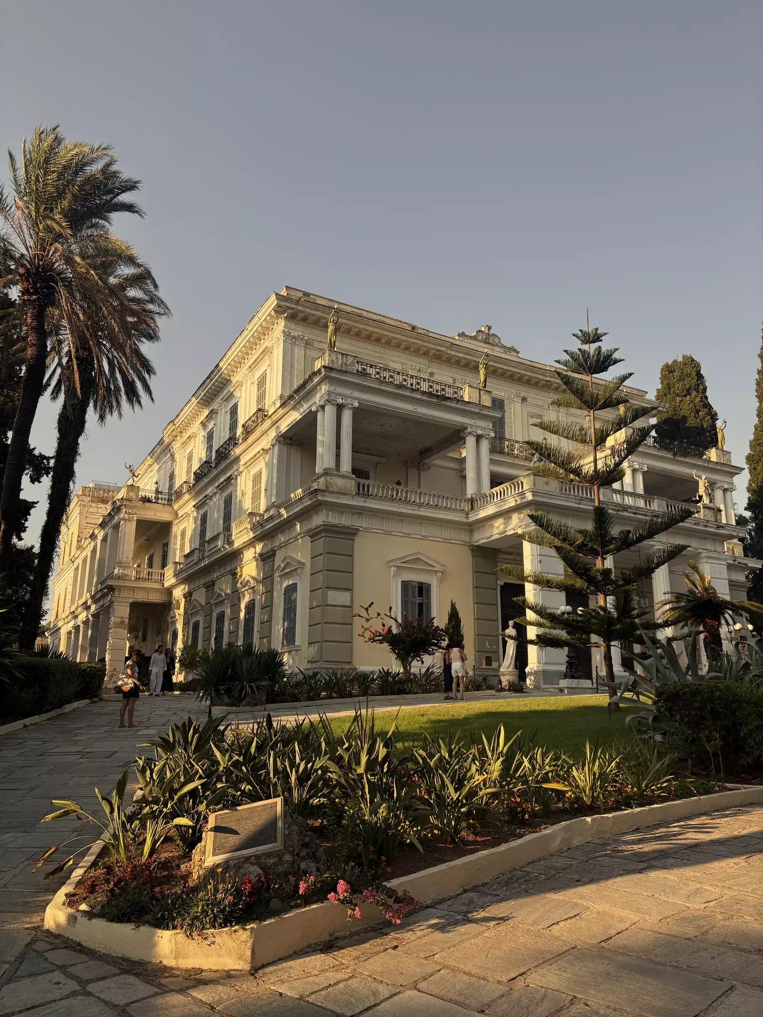 Neoklassieke voorgevel van het Achilleion-paleis op Corfu tussen palmbomen en bloeiende tuin