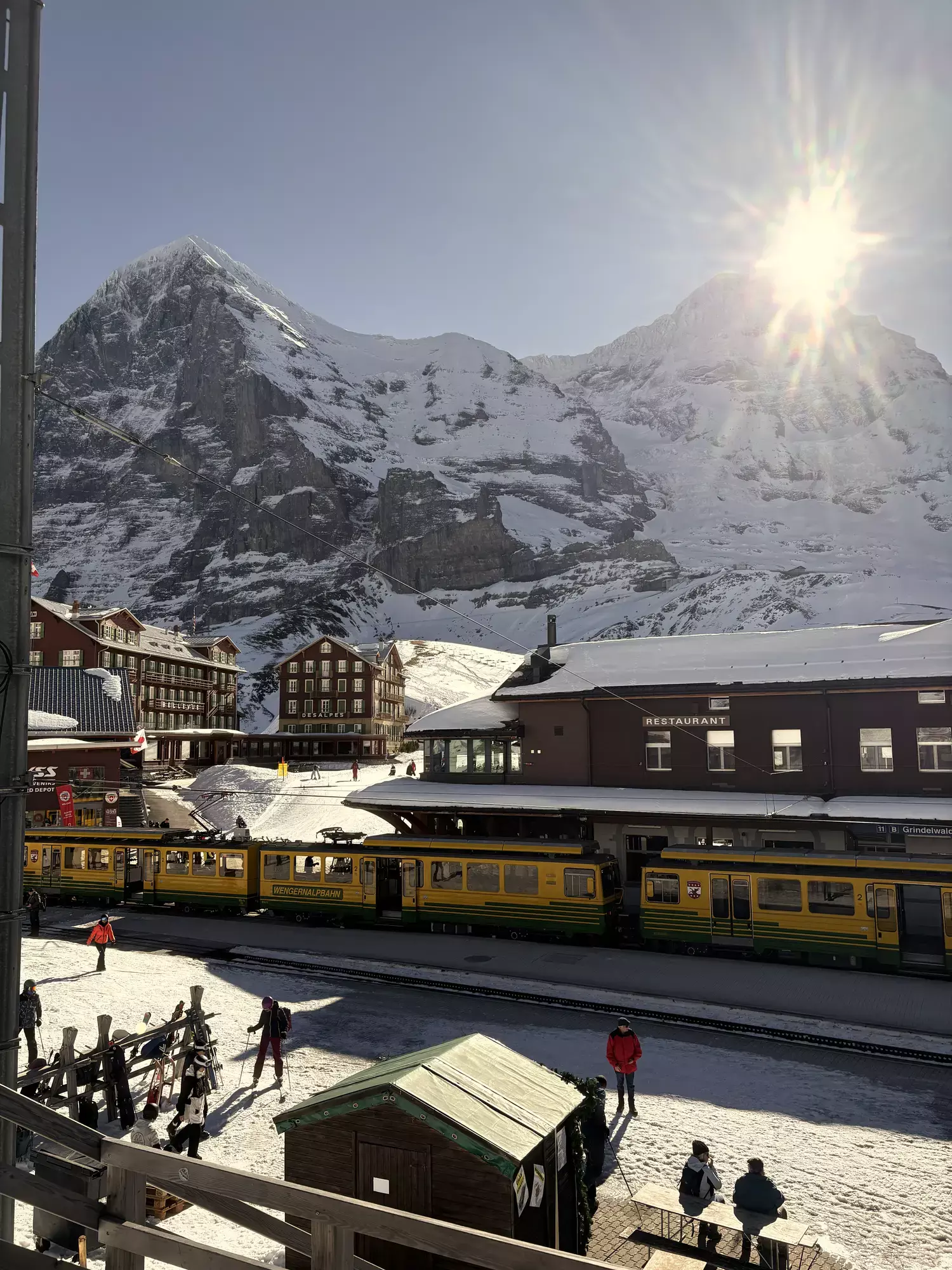 De Eiger met zijn noordwand boven station Kleine Scheidegg, met treinen van de Wengernalpbahn en wintersporters in de sneeuw