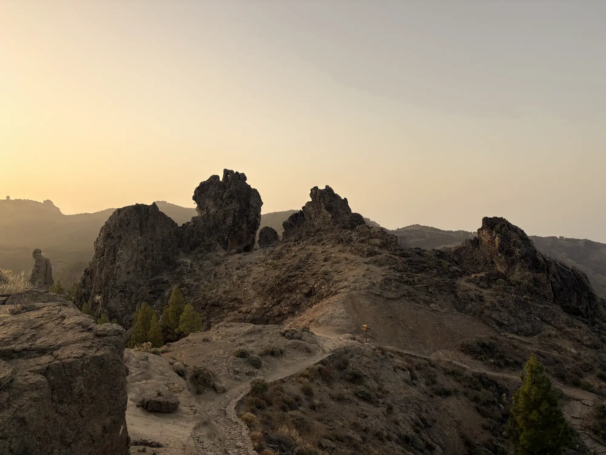 Donkere rotsformaties en een wandelpad tegen een gouden lucht bij zonsondergang Roque Nublo