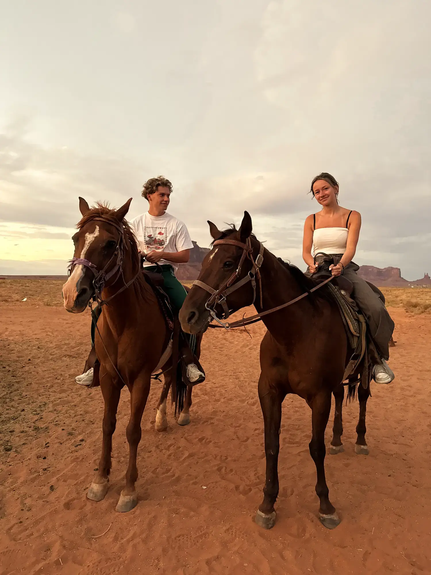 Jonge man en vrouw te paard op het rode zand van Monument Valley met de kenmerkende rotsformaties op de achtergrond