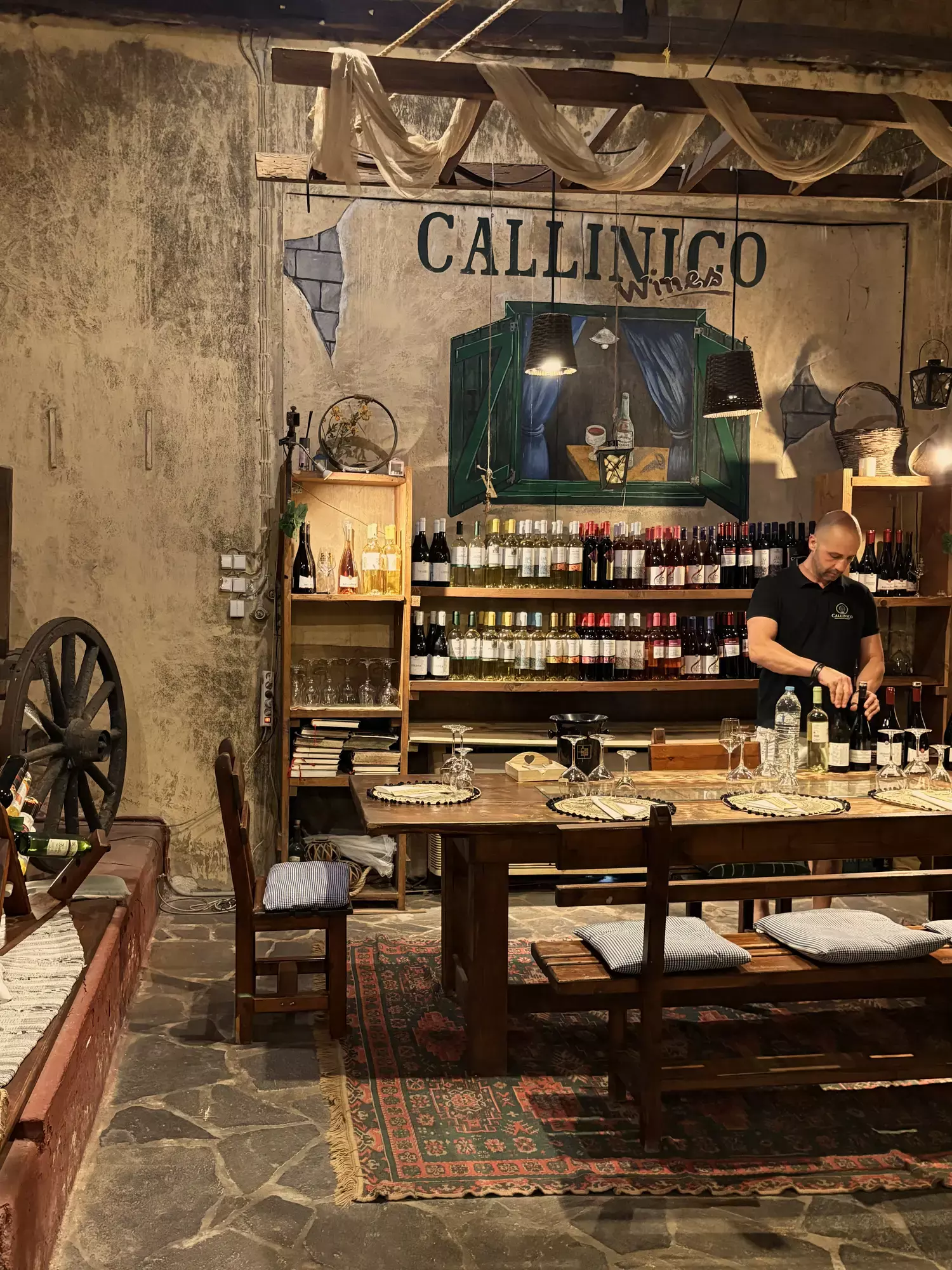 Gastheer achter de bar van Callinico voor een wand met wijnflessen en het Callinico-logo