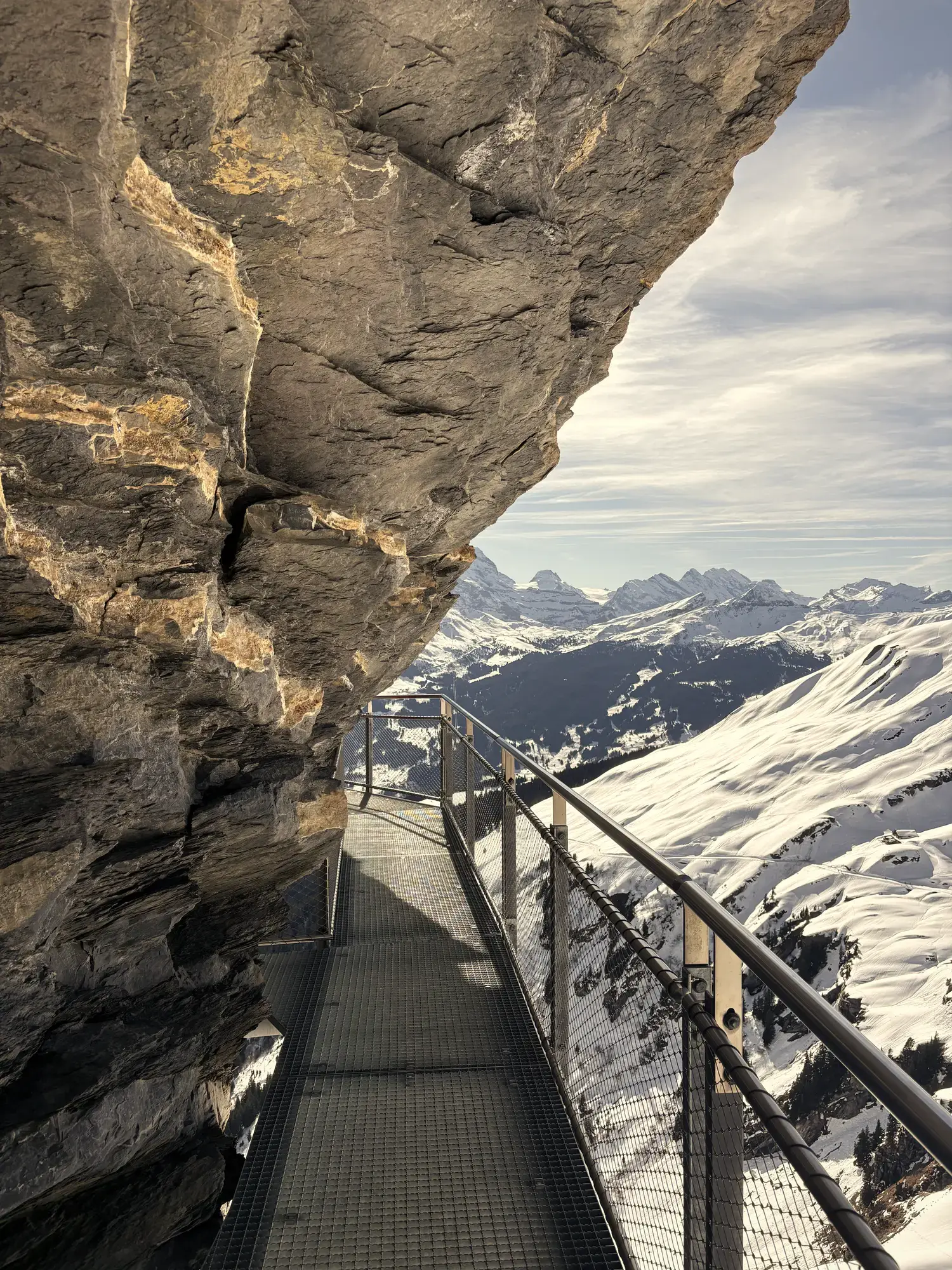 Stalen loopbrug van de First Cliff Walk langs een rotswand met uitzicht op besneeuwde bergtoppen boven Grindelwald