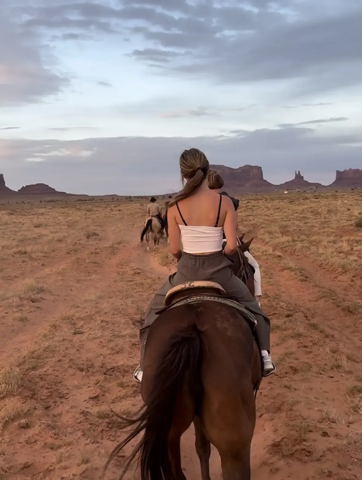 Ruiters rijden achter een gids over een zandpad door Monument Valley, met de rode buttes aan de horizon in het avondlicht