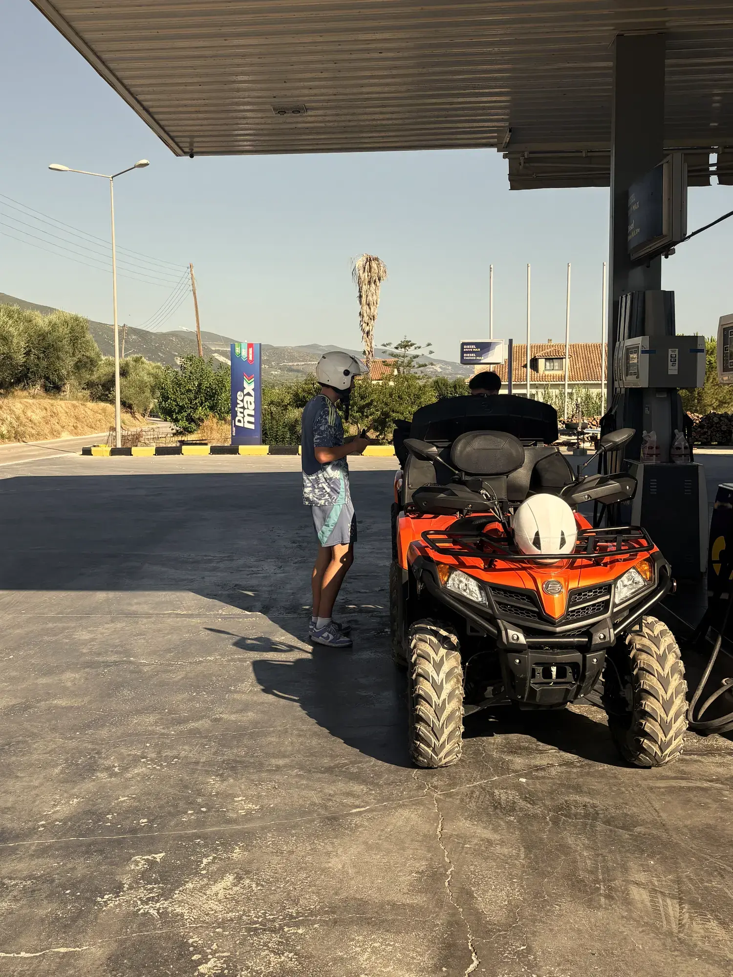 Gehuurde oranje quad met witte helm op het rek staat bij de pomp van een tankstation op Zakynthos