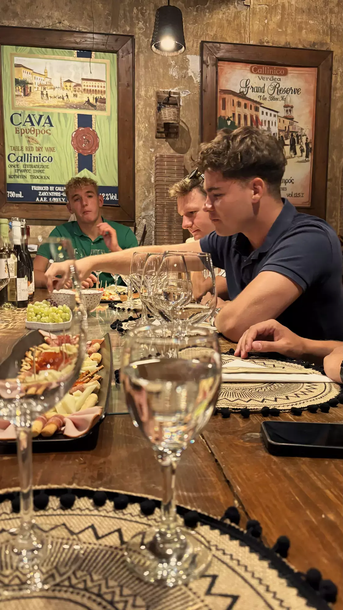 Vrienden aan een lange tafel met wijnglazen, druiven en een plank vleeswaren bij Callinico