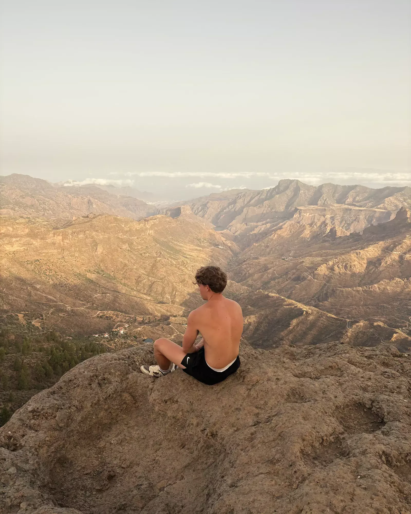 Wandelaar zit op een rots en kijkt uit over diepe bergdalen van Gran Canaria in warm licht Roque Nublo