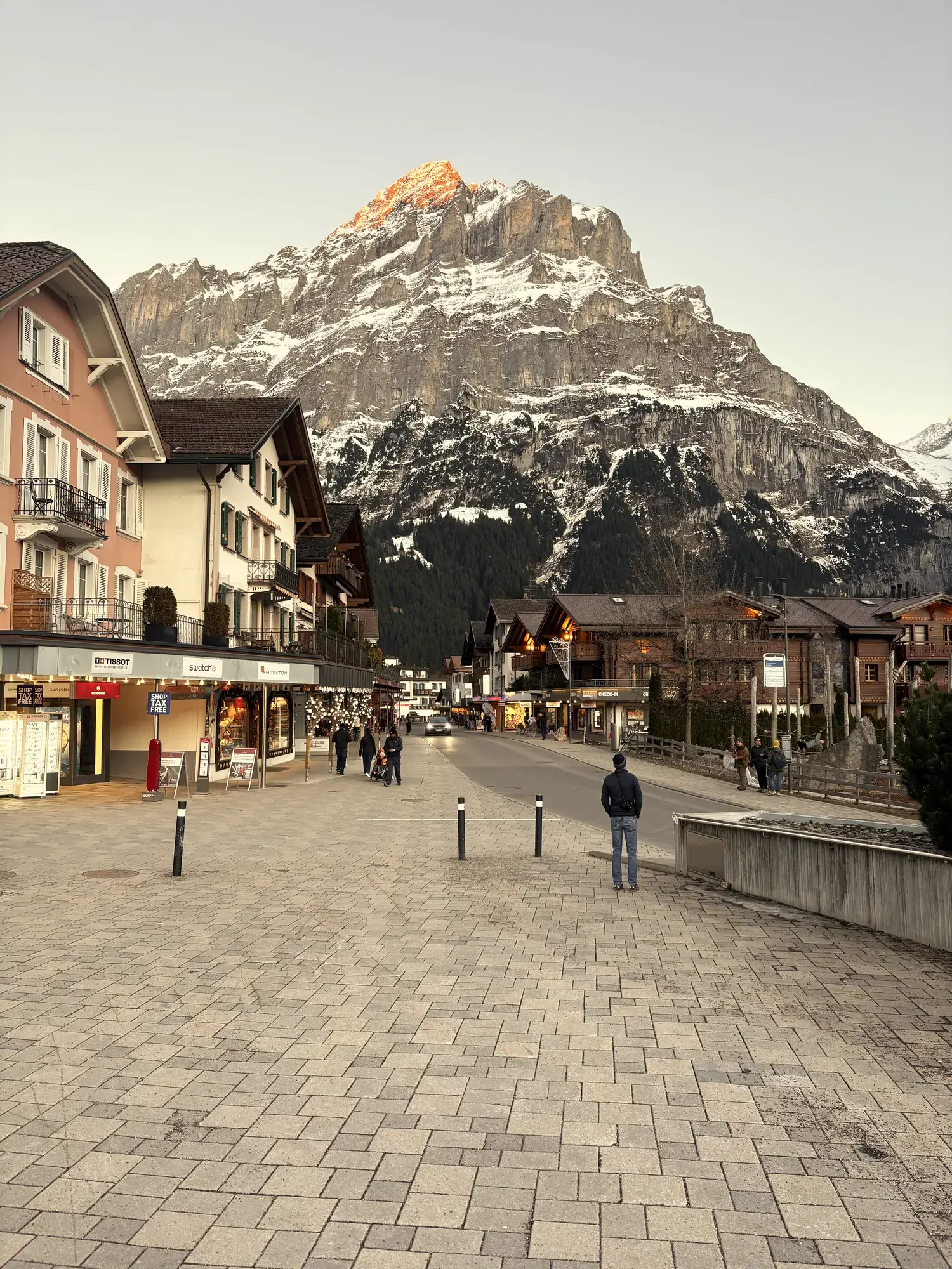 De Dorfstrasse in Grindelwald met winkels en chalets, met de Wetterhorn in het laatste avondlicht aan het eind van de straat